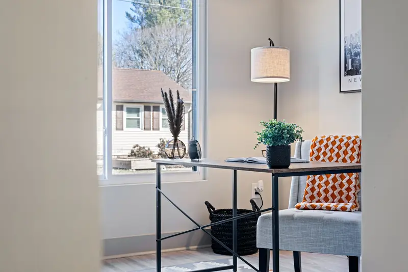 Bright modern home office with a minimalist desk, lamp, and cozy blanket by the window