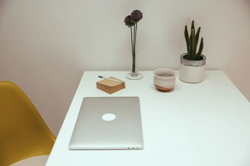 A clean and modern minimalist workspace featuring a laptop, cactus, and decorative elements on a white desk