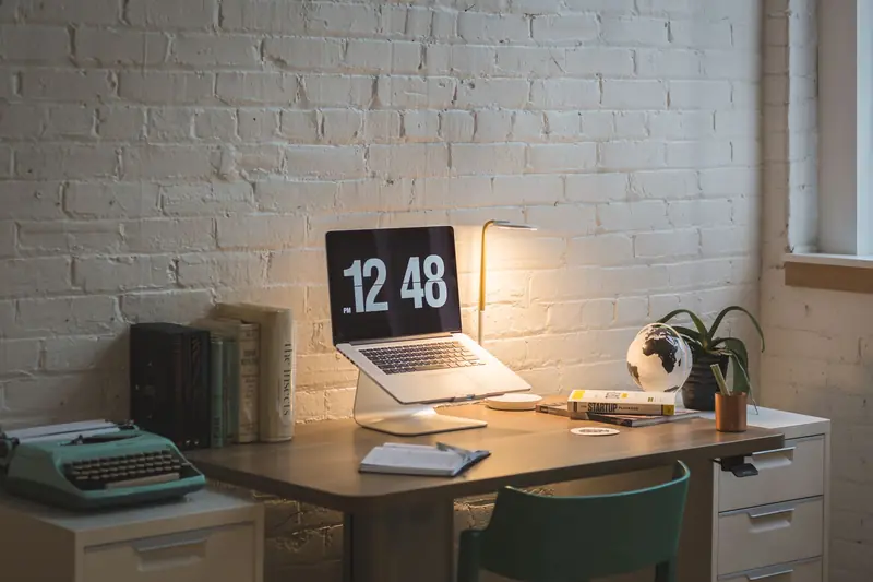 A well-organized workspace featuring a laptop, books, and a lamp on a wooden desk