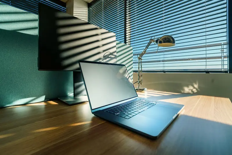 A clean, sunlit office desk with a modern laptop and monitor, perfect for business or corporate settings