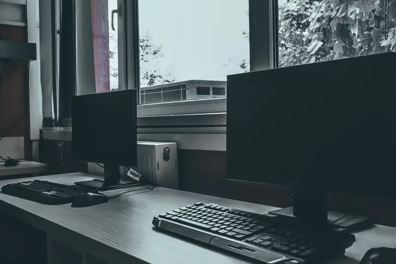 Contemporary computers with black screens placed on desk near window in classroom or office