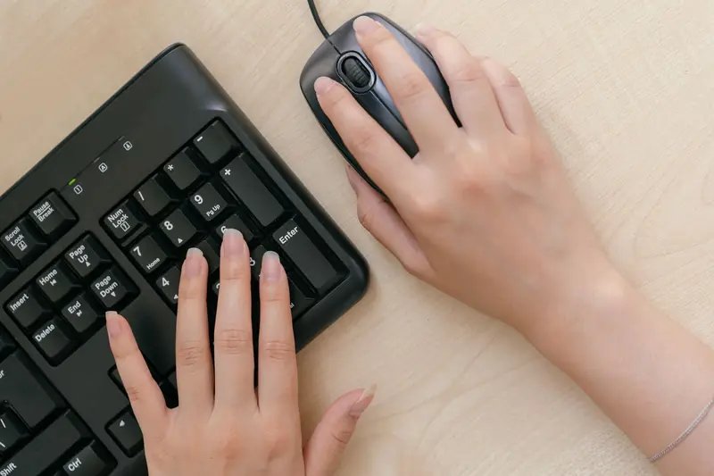 Close-up of hands on a keyboard and mouse, highlighting office work setup