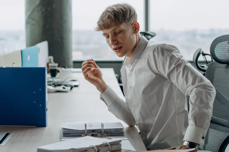 Man in white shirt sitting at office desk reading documents, modern workspace