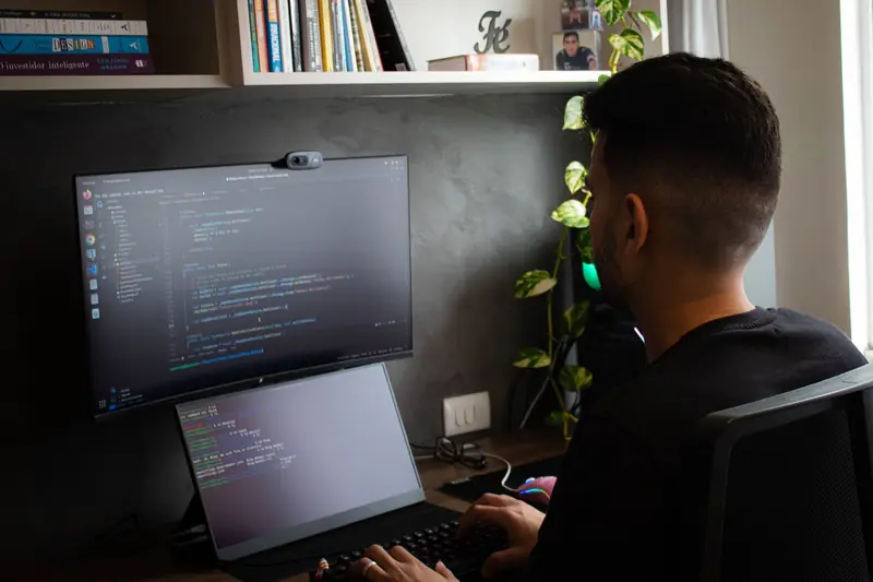 A programmer coding on a laptop and monitor in a stylish office setup