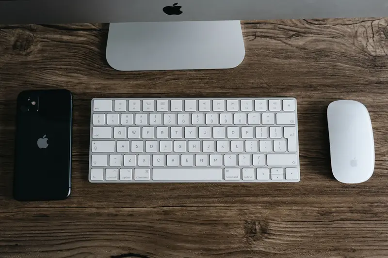 A minimalist workspace featuring a smartphone, keyboard, and mouse on a wooden desk