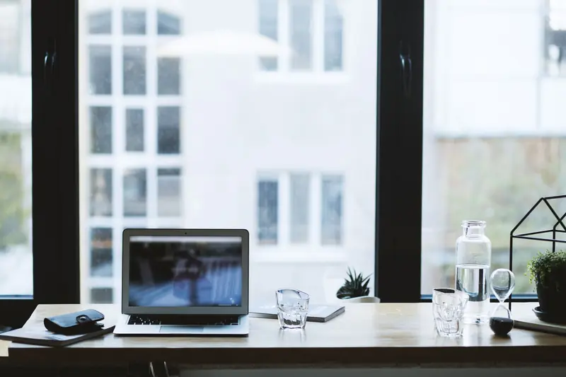 Sleek office desk setup featuring a laptop, glass of water, and open window view
