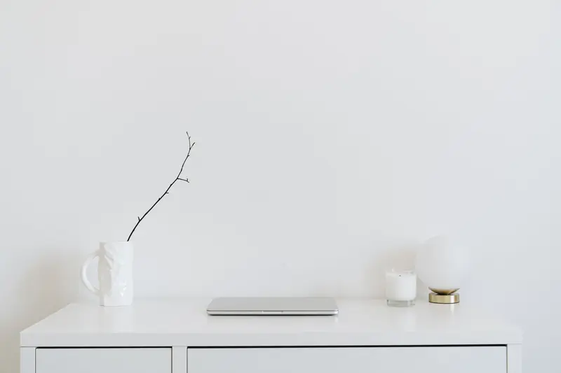 A clean, minimalistic workspace featuring a white desk, laptop, and decorative items, perfect for modern design inspiration