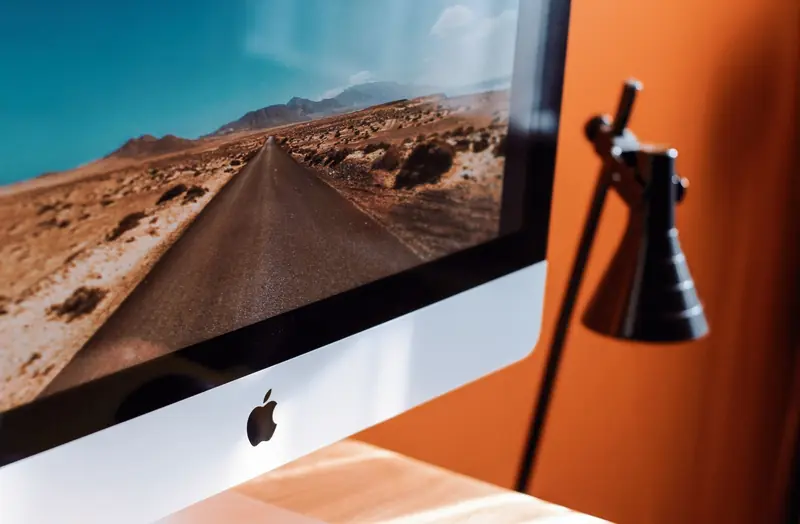 A sleek modern workspace featuring an iMac displaying a desert road and a stylish desk lamp